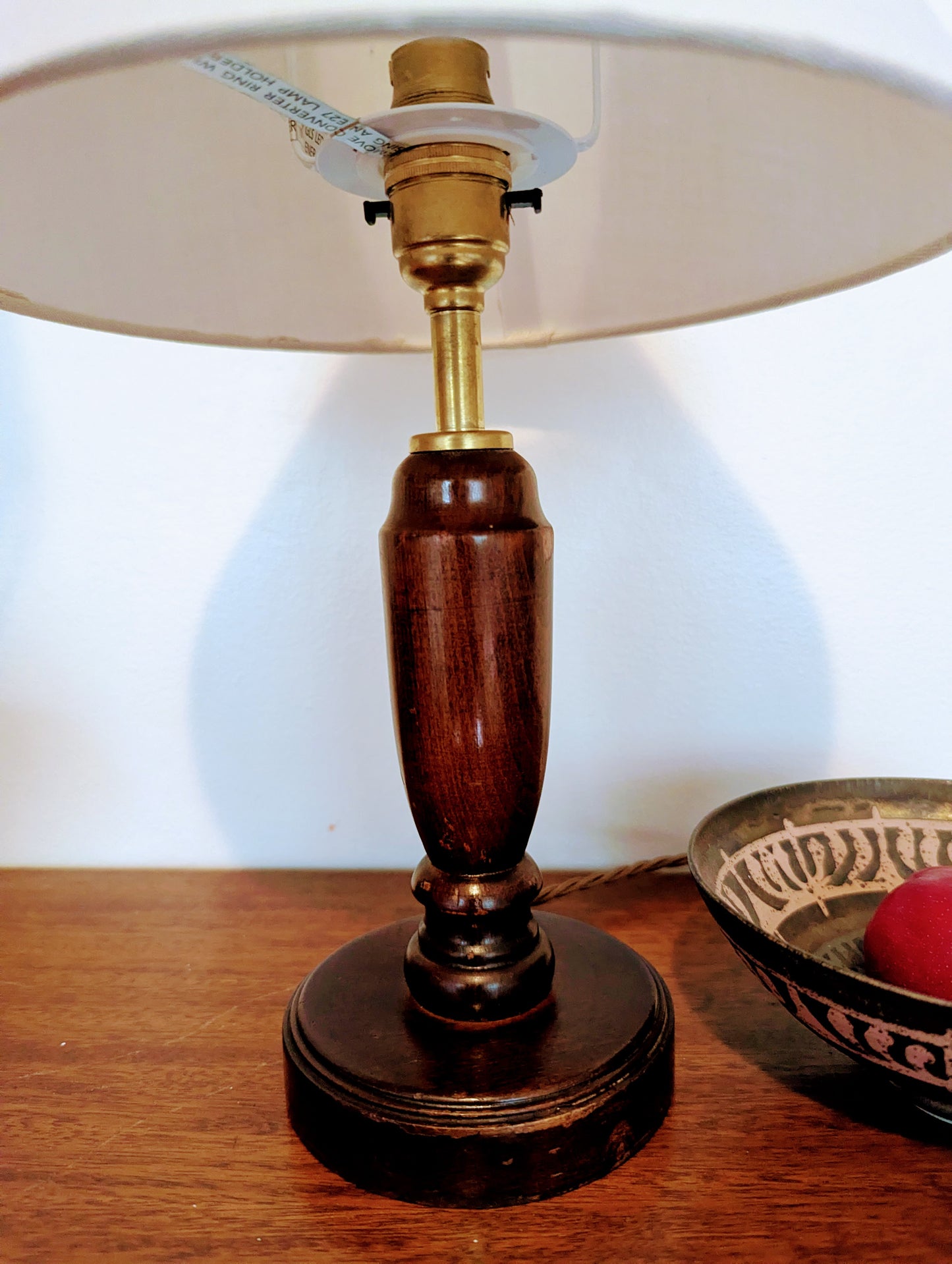 Mahogany turned table lamp with a wooden base and linen shade on a wooden surface.