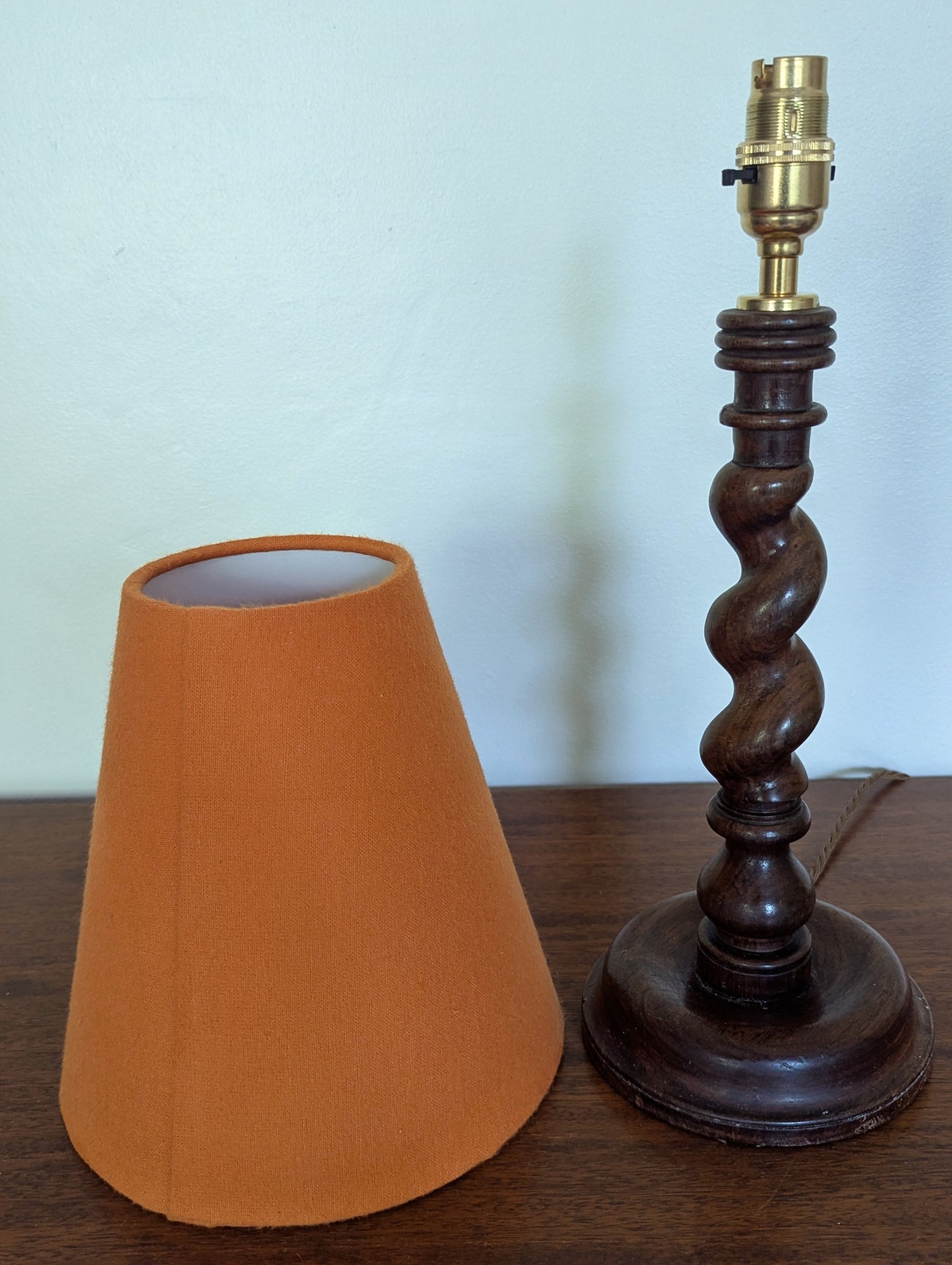 Mahogany barley twist table lamp with circular base and a brushed cotton orange shade on a wooden surface.