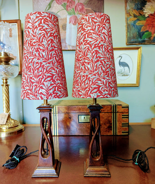 Two arts & crafts movement table lamps with red and white william morris patterned shades on a wooden surface.