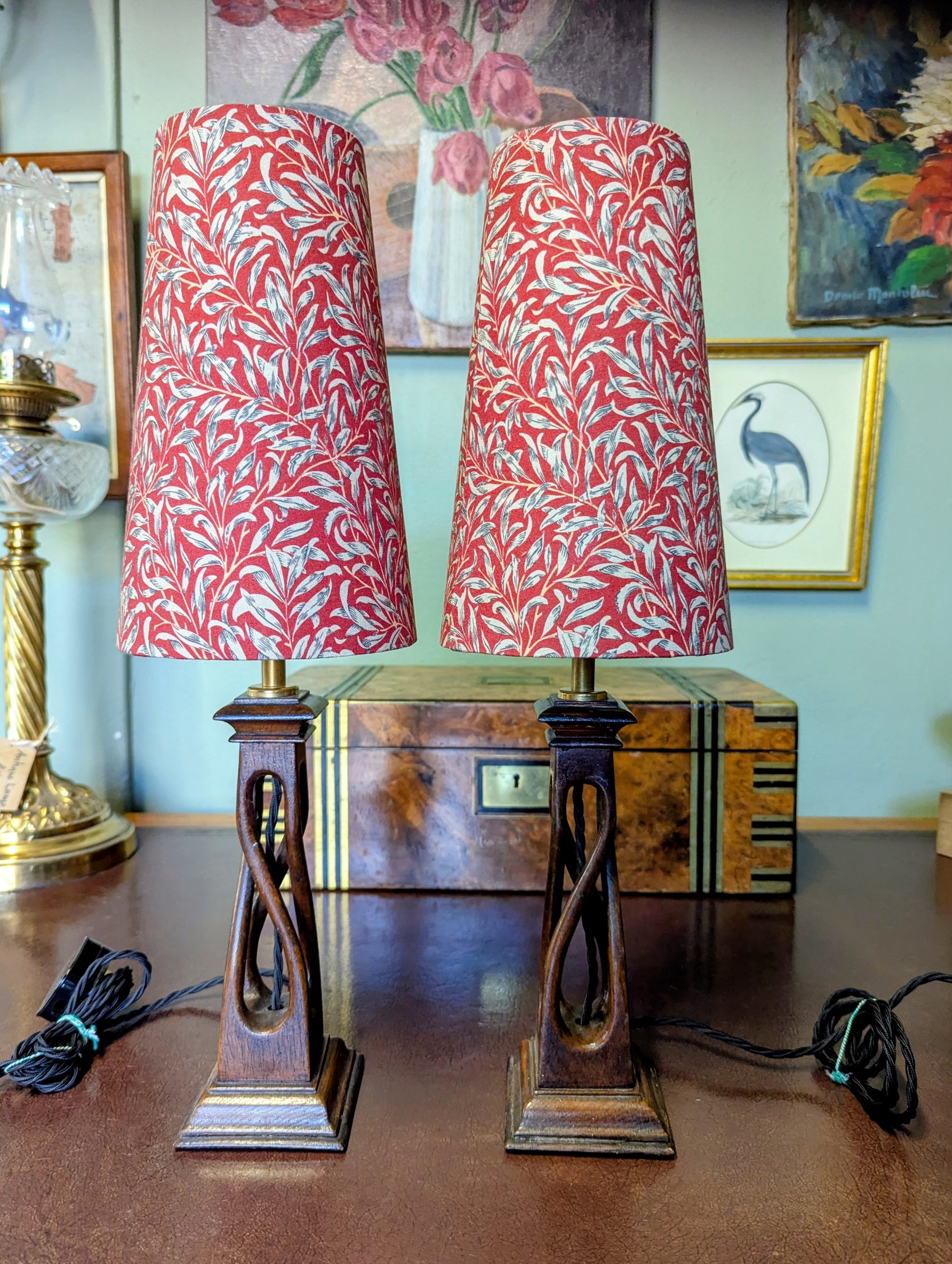 Two arts & crafts movement table lamps with red and white william morris patterned shades on a wooden surface.