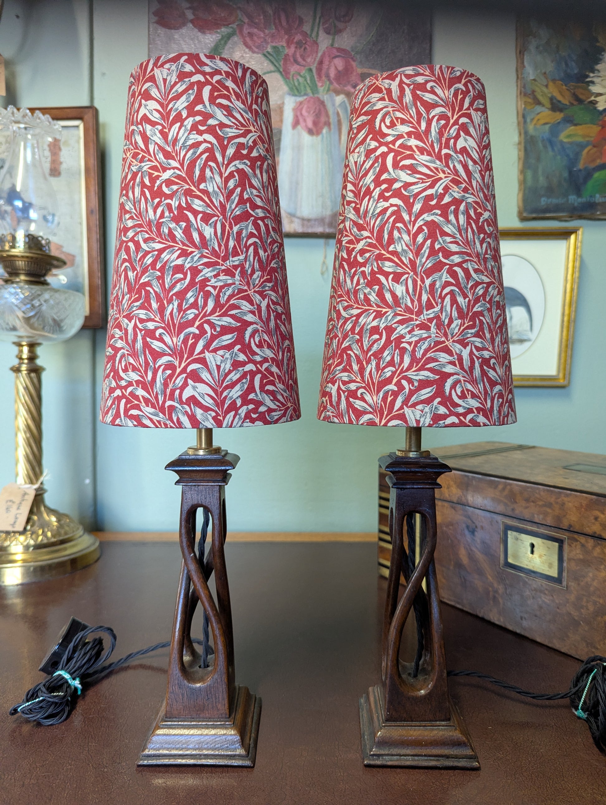 Two arts & crafts movement table lamps with red and white william morris patterned shades on a wooden surface.