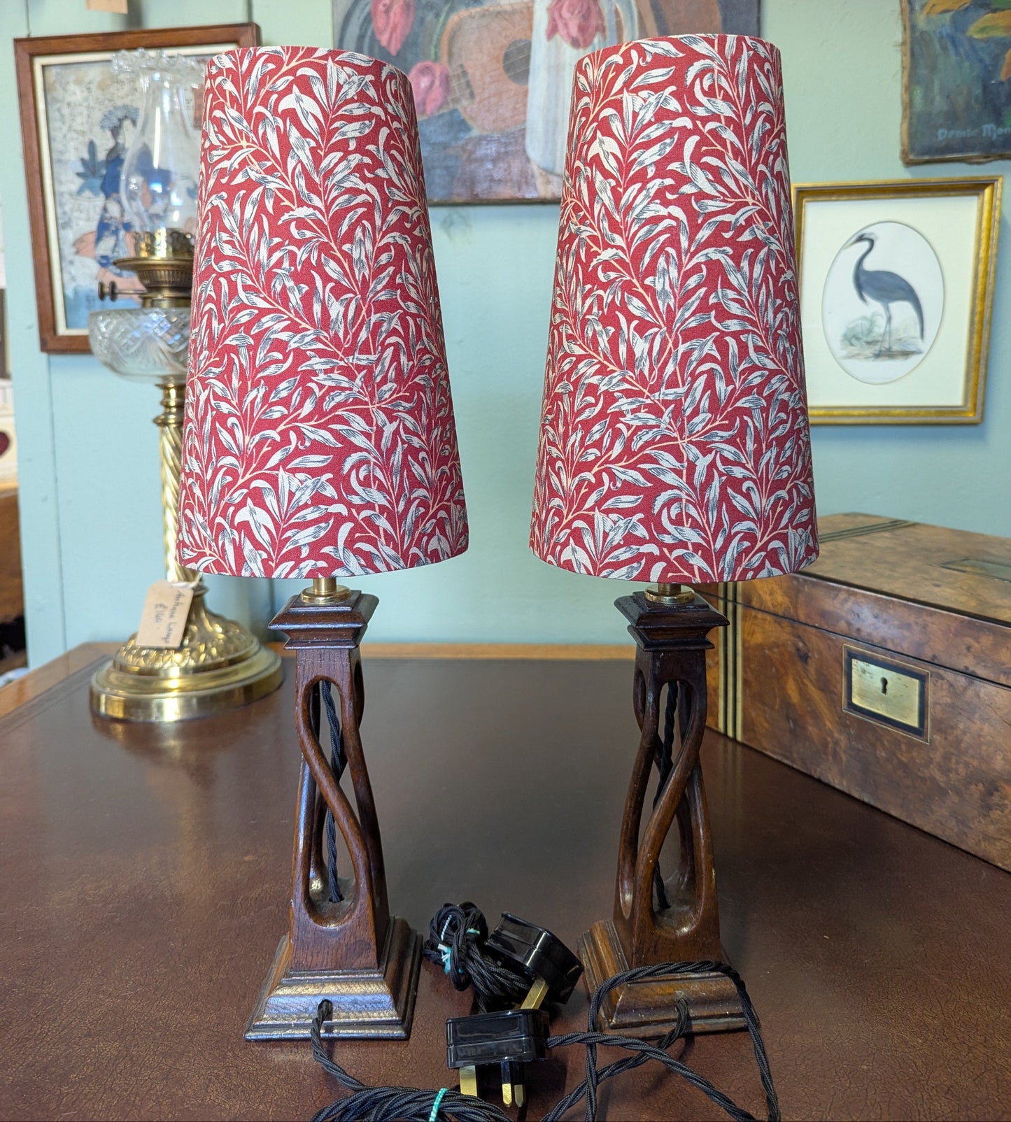 Two arts & crafts movement table lamps with red and white william morris patterned shades on a wooden surface.