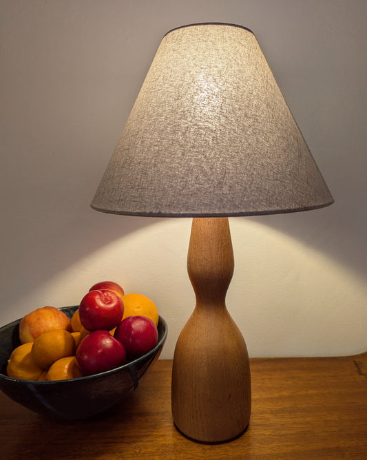 Wooden Danish Mid 20th Century table lamp with a gray lampshade on a wood surface with a bowl of fruit