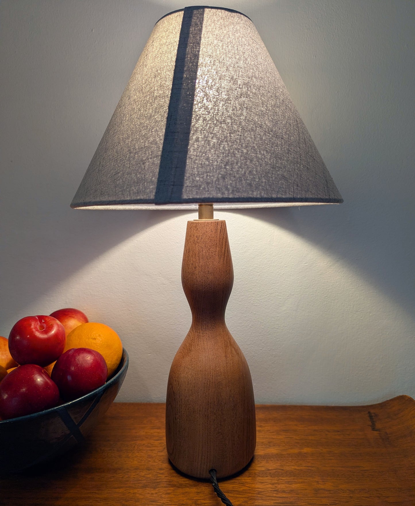 Wooden Danish Mid 20th century table lamp with a textured white shade on a wooden table next to a bowl of fruits.