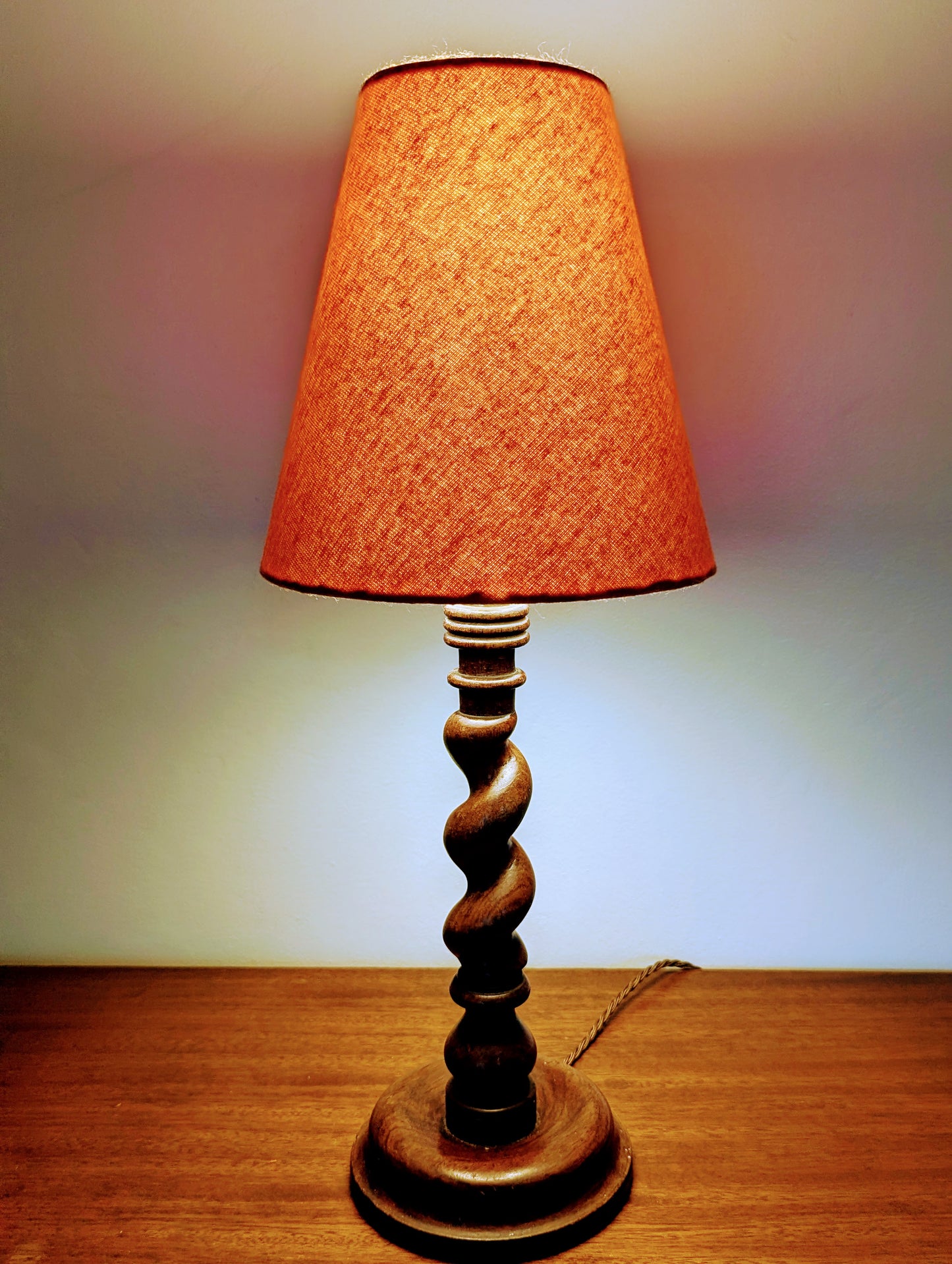 Mahogany barley twist table lamp with circular base and a brushed cotton orange shade on a wooden surface.