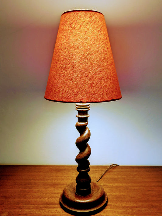Mahogany barley twist table lamp with circular base and a brushed cotton orange shade on a wooden surface.