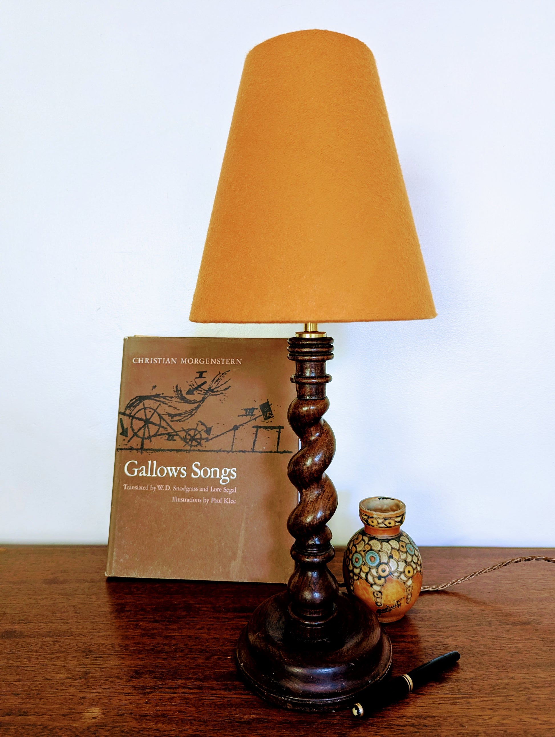 Mahogany barley twist table lamp with circular base and a brushed cotton orange shade on a wooden surface.