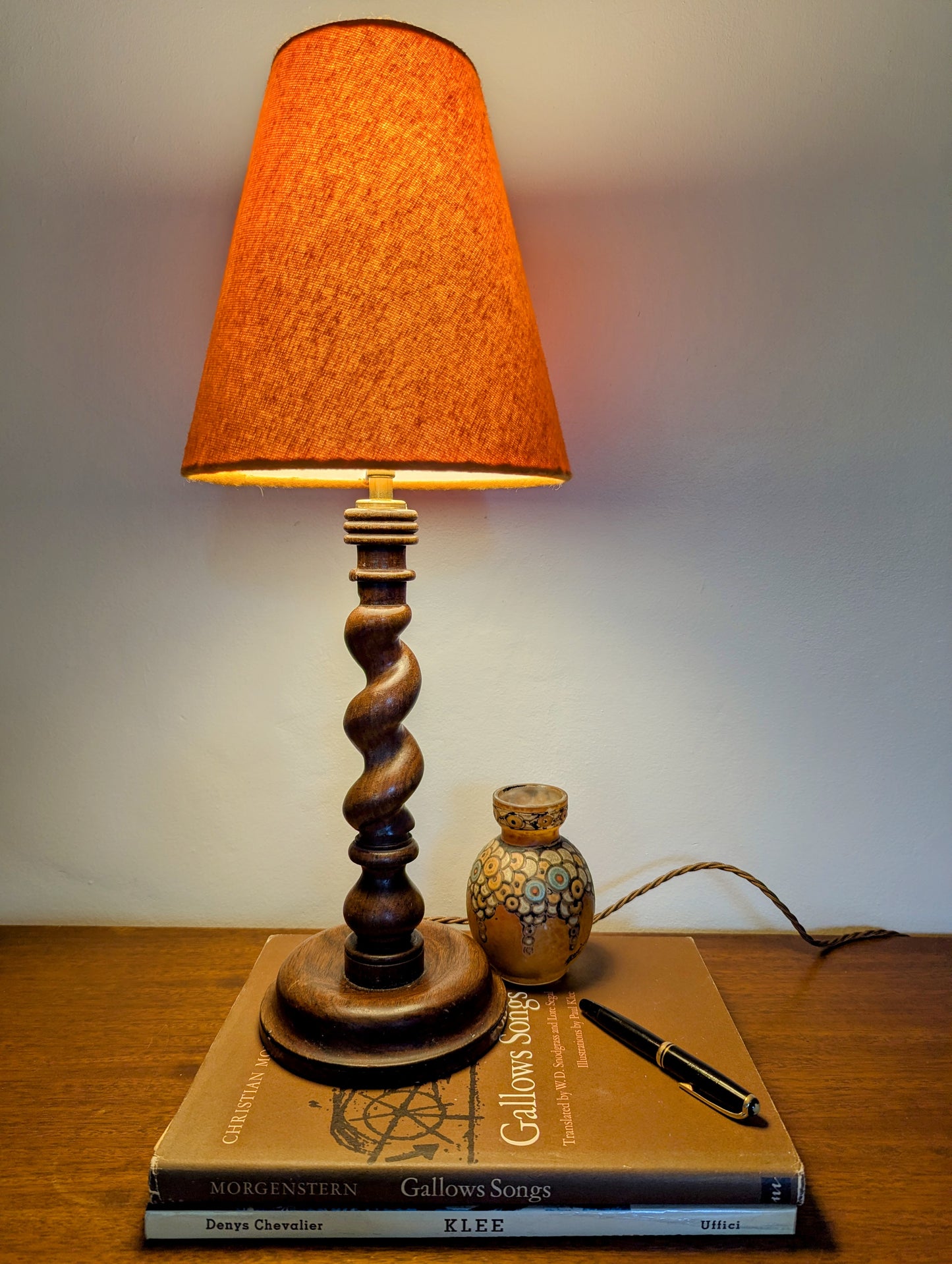Mahogany barley twist table lamp with circular base and a brushed cotton orange shade on a wooden surface.