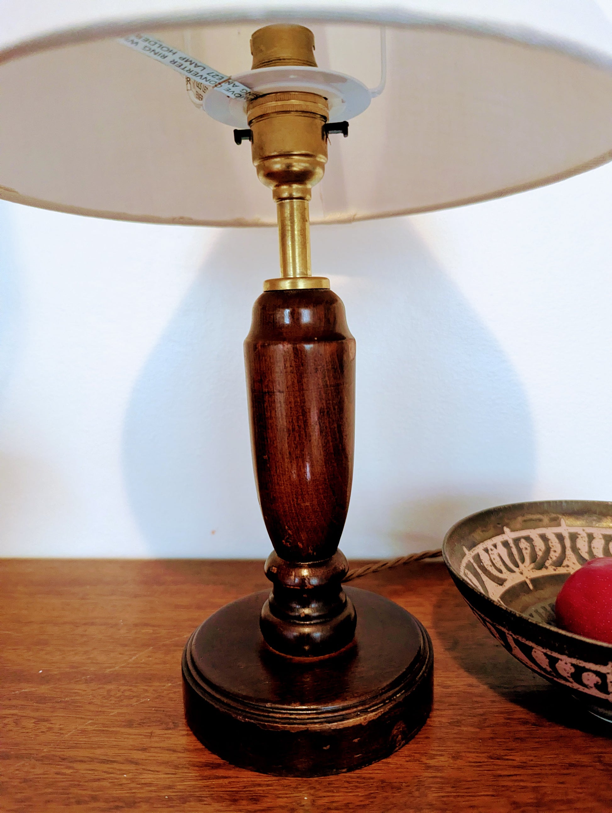 Mahogany turned table lamp with a wooden base and linen shade on a wooden surface.