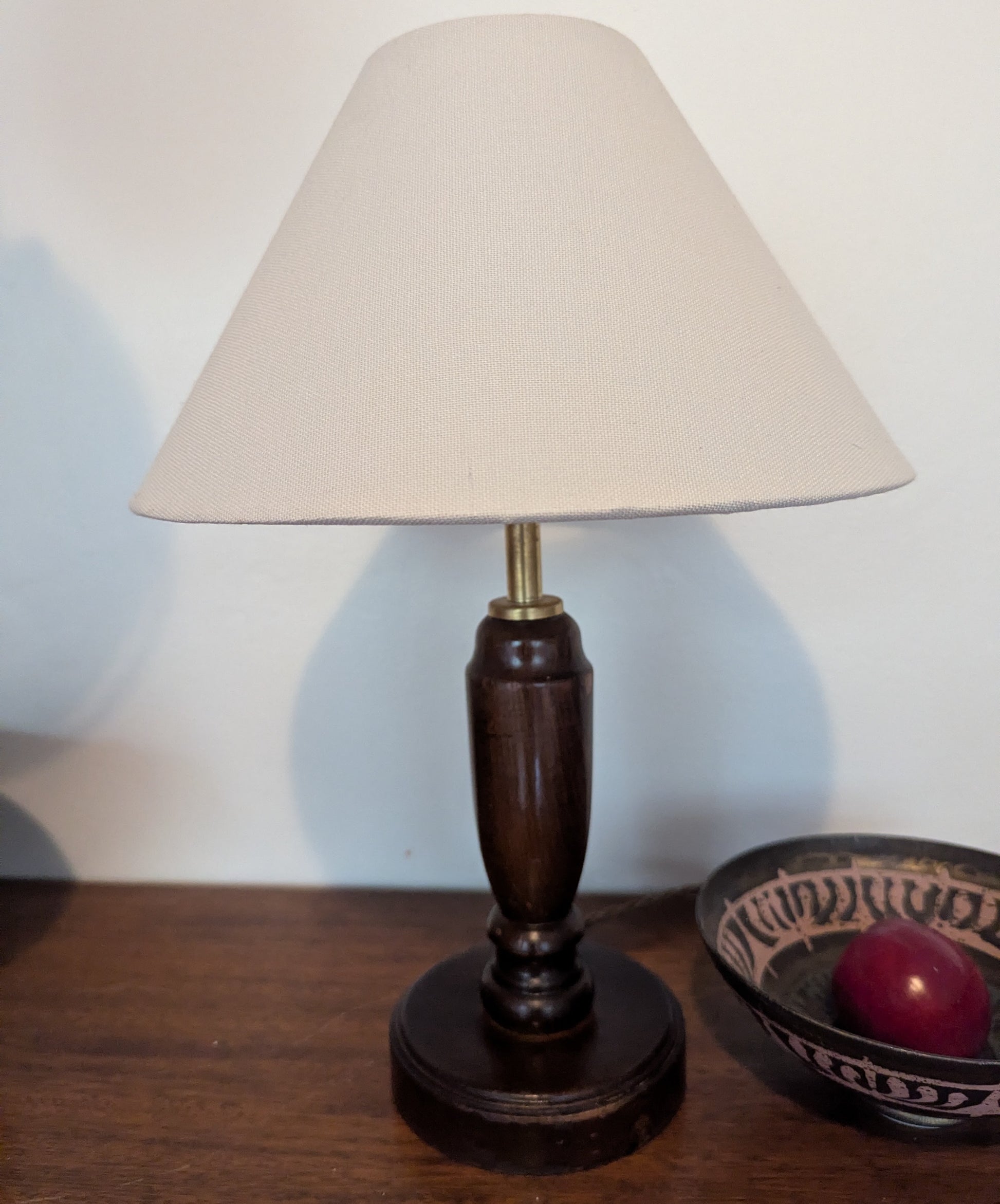 Mahogany turned table lamp with a wooden base and linen shade on a wooden surface.