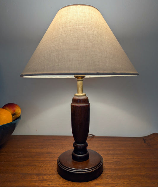 Mahogany turned table lamp with a wooden base and linen shade on a wooden surface.