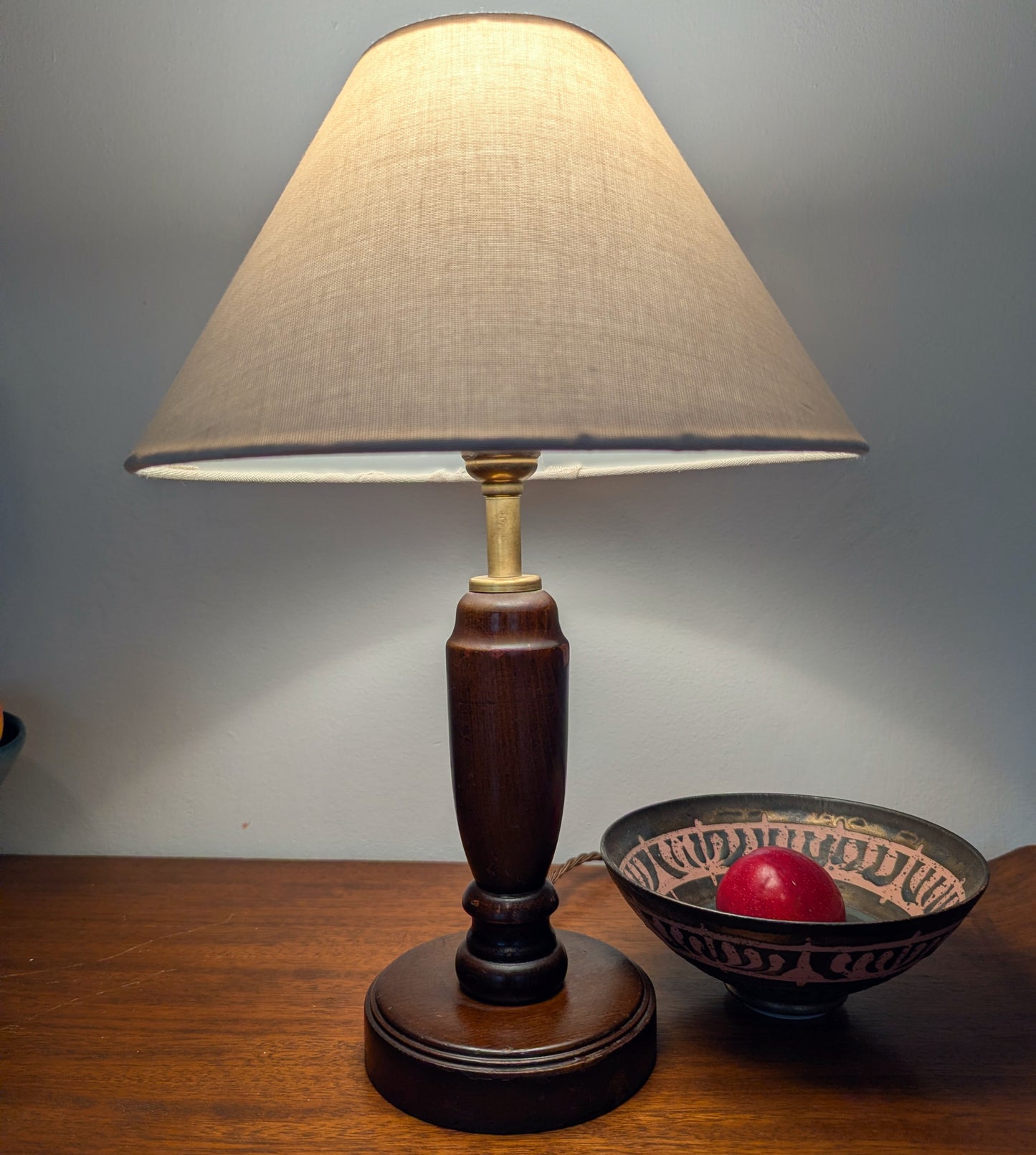 Mahogany turned table lamp with a wooden base and linen shade on a wooden surface.