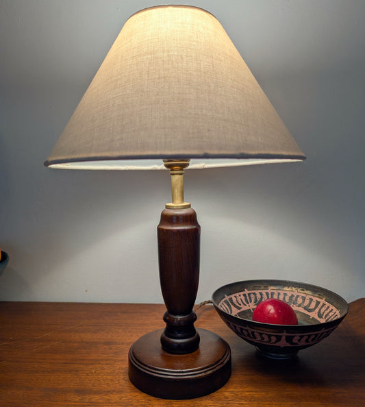 Mahogany turned table lamp with a wooden base and linen shade on a wooden surface.